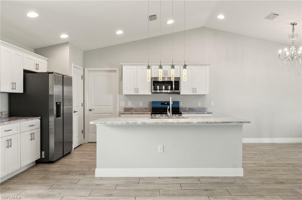 Kitchen featuring a central island with a sink, white cabinetry, integrated stainless steel appliances, and wood-finish flooring