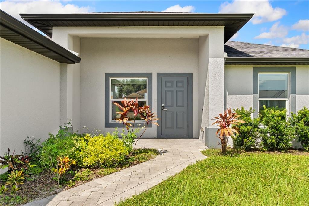 Stucco exterior featuring a covered entry, gray paneled door, and framed windows