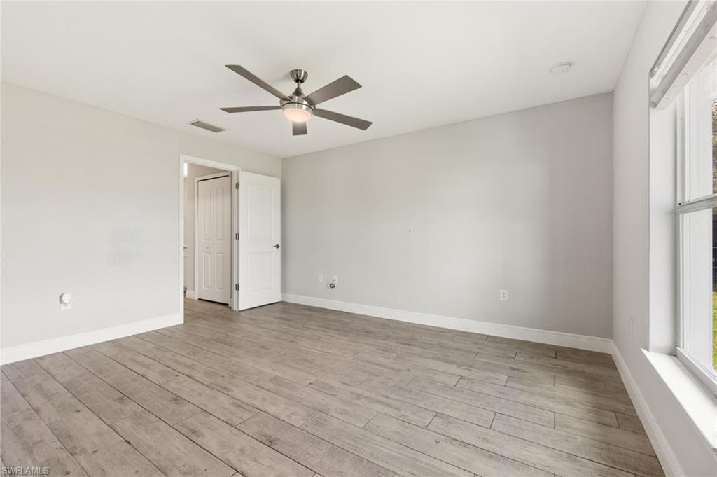 Spacious room featuring wood-finish flooring, light gray walls, a ceiling fan with integrated lighting, and a large window