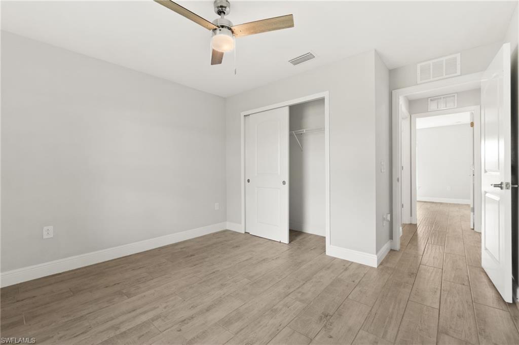 Bedroom featuring wood-finish flooring, a ceiling fan with integrated lighting, a sliding closet door, and crisp white baseboards