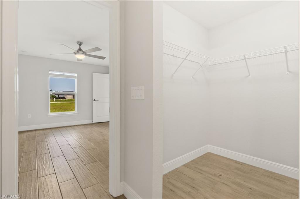 Bedroom featuring a ceiling fan with integrated lighting, wood-finish flooring, and a window overlooking a green expanse