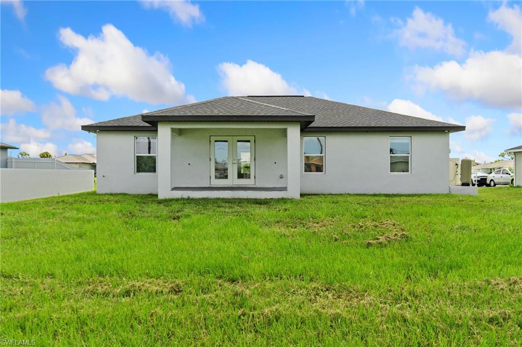 Rear exterior featuring a covered patio, double French doors, multiple windows, and a fenced perimeter