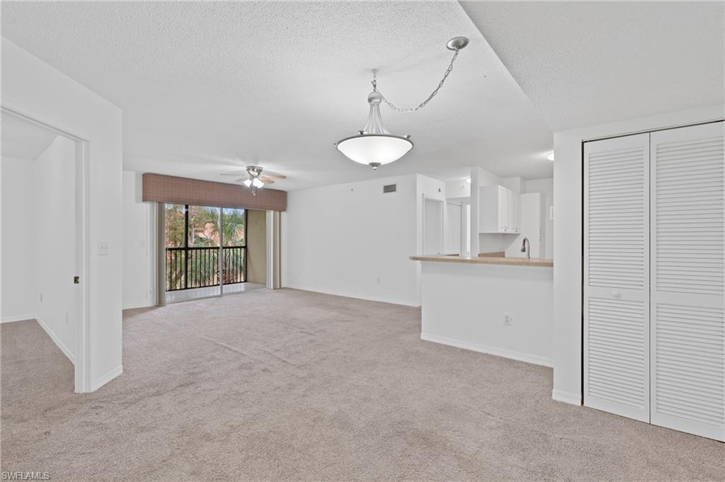 Unfurnished living room featuring light carpet, baseboards, a ceiling fan, a textured ceiling, and a sink