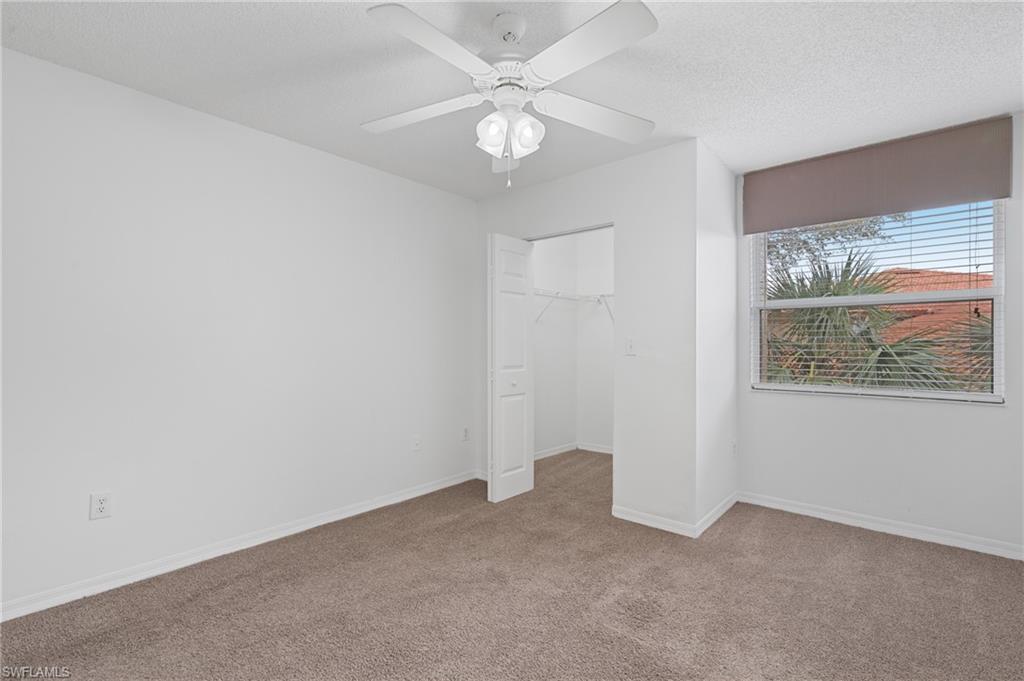 Unfurnished bedroom featuring baseboards, light colored carpet, a walk in closet, a textured ceiling, and a closet
