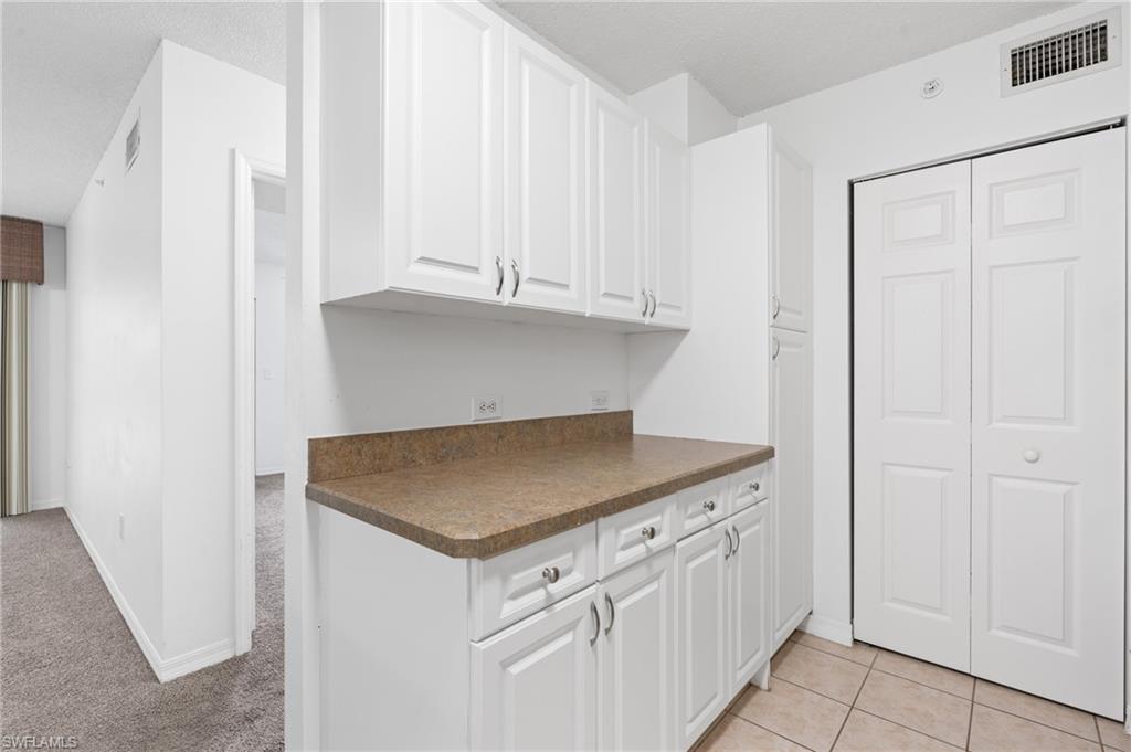 Kitchen featuring light tile patterned floors, dark countertops, visible vents, and white cabinetry