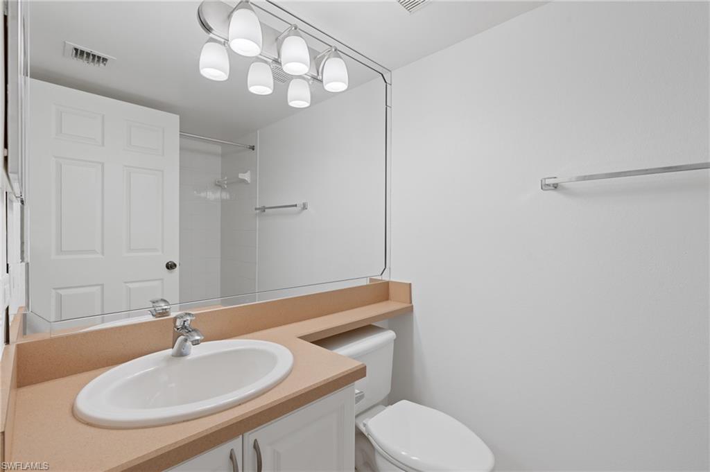 Full bathroom with toilet, visible vents, walk in shower, and vanity