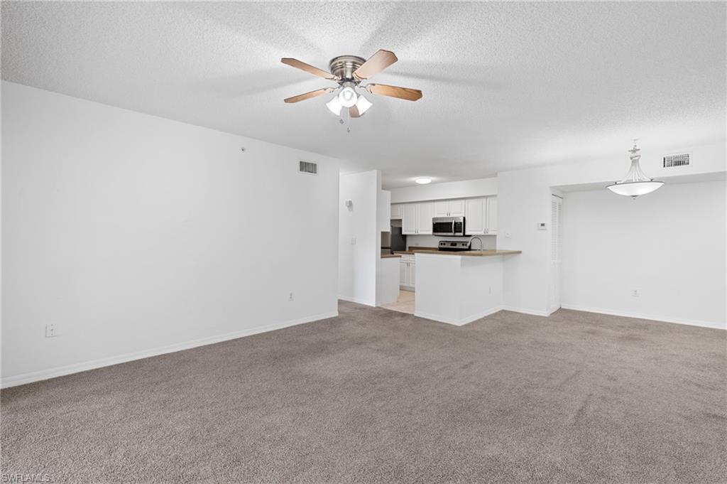 Unfurnished living room with a ceiling fan, light colored carpet, visible vents, and a textured ceiling