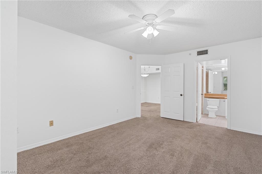 Unfurnished bedroom with a textured ceiling, connected bathroom, light colored carpet, visible vents, and baseboards