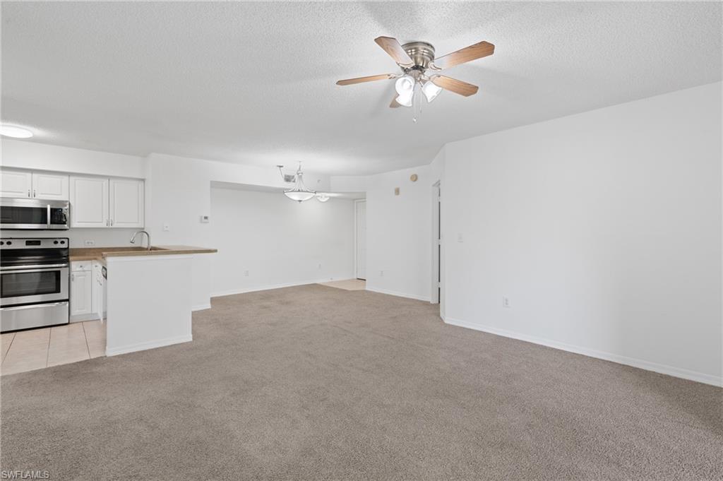 Unfurnished living room with light carpet, baseboards, a textured ceiling, and ceiling fan with notable chandelier