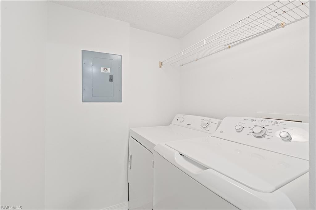 Laundry room with laundry area, electric panel, washer and clothes dryer, and a textured ceiling
