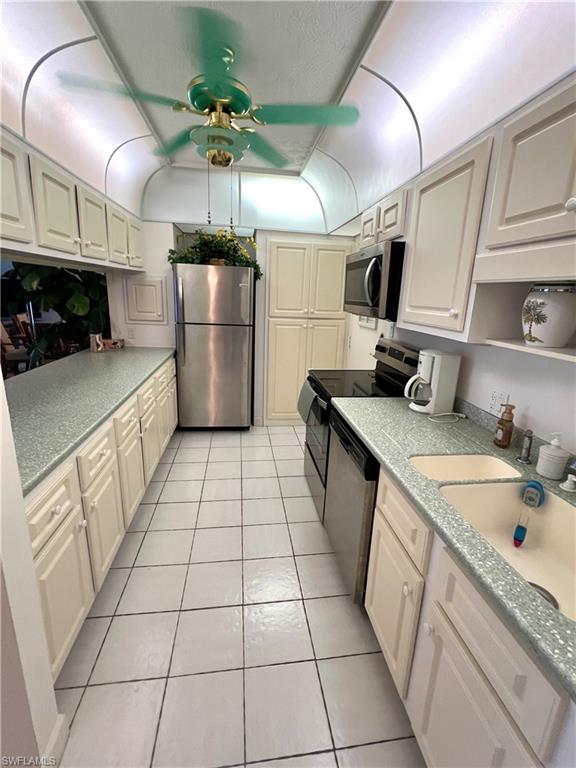 Galley kitchen featuring plenty of cabinetry, solid countertops, white tile flooring, stainless steel appliances, and a ceiling fan
