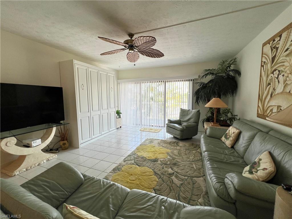 Living area featuring white tile flooring, a tropical-style ceiling fan, and Murphy bed
