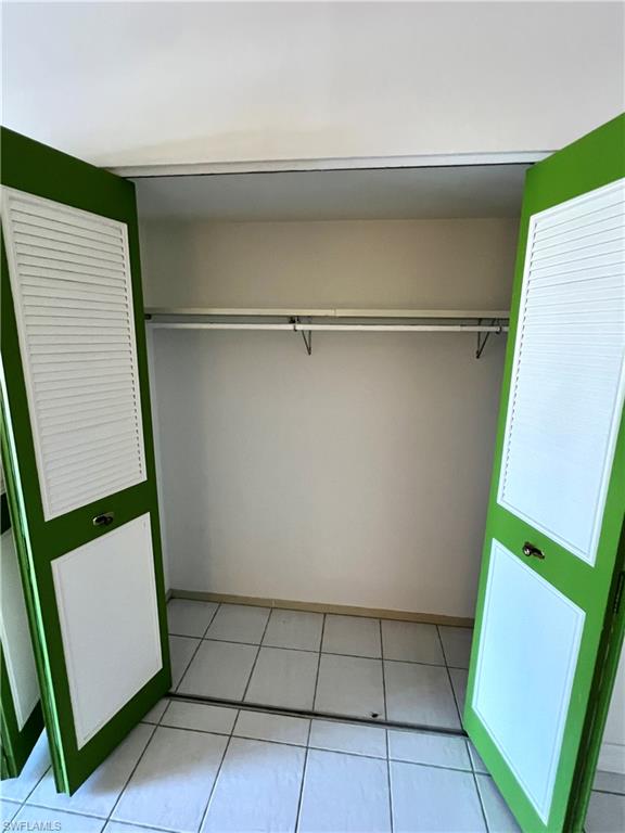 One of two large bedroom closets featuring bi-fold doors with louvered and panel details, a single hanging rod, and white tile flooring
