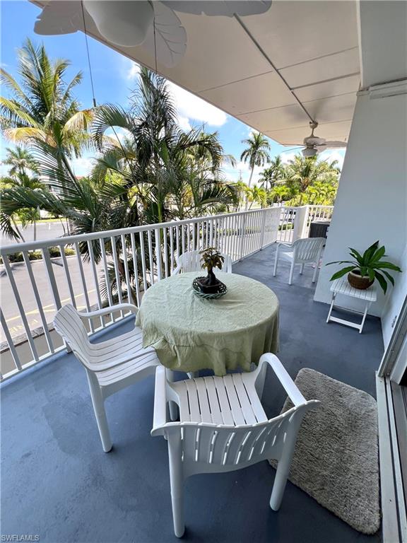 Expansive balcony featuring a white railing, ceiling fan, palm tree scenery, and a sliding glass door