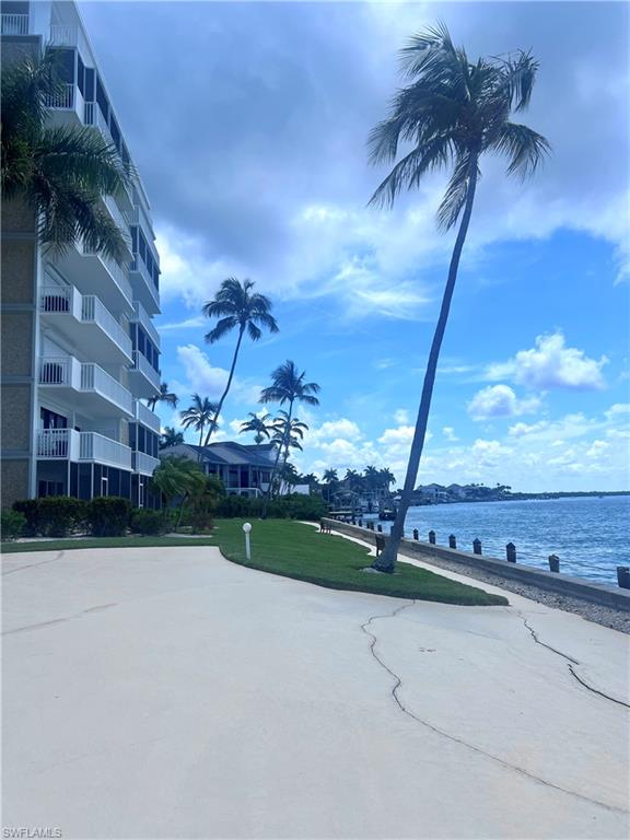 Waterfront property featuring a multi-story building with private balconies, mature palm trees, a concrete seawall, and a manicured lawn