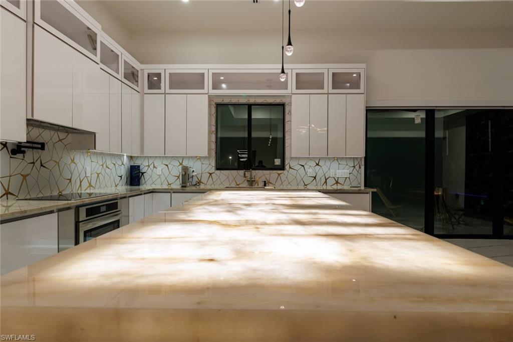 Kitchen with backsplash, white cabinetry, glass insert cabinets, light stone counters, and oven