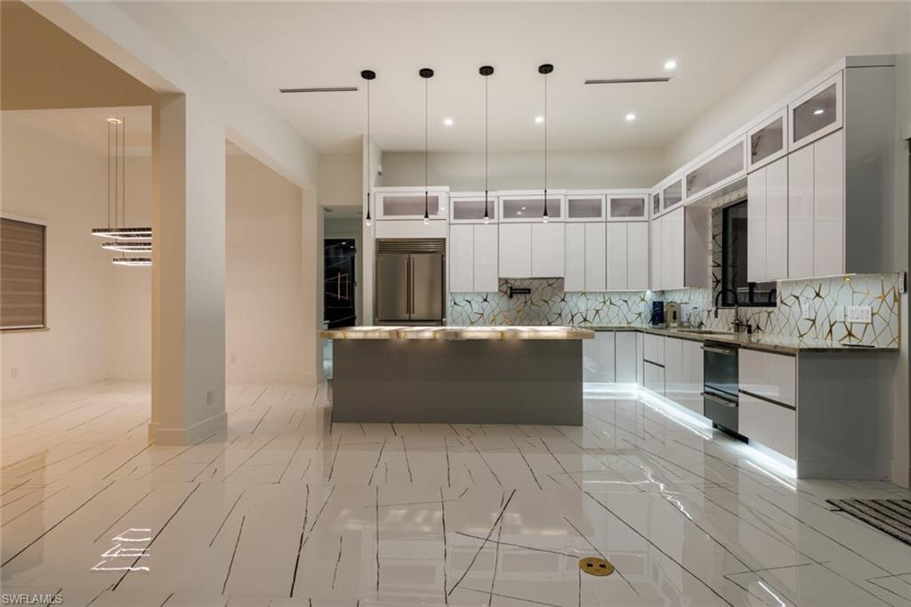 Kitchen with decorative light fixtures, a kitchen island with cristallo countertops, glass insert cabinets, white cabinets, and modern cabinets