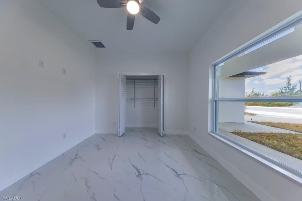 Spacious room featuring white walls, marble-look tile flooring, and a ceiling fan with integrated lighting
