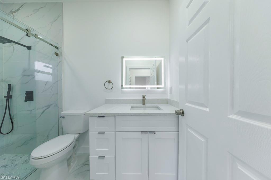 Modern bathroom featuring a glass-enclosed shower with a rain showerhead, a white vanity with a quartz countertop, an illuminated mirror, and sleek white cabinetry
