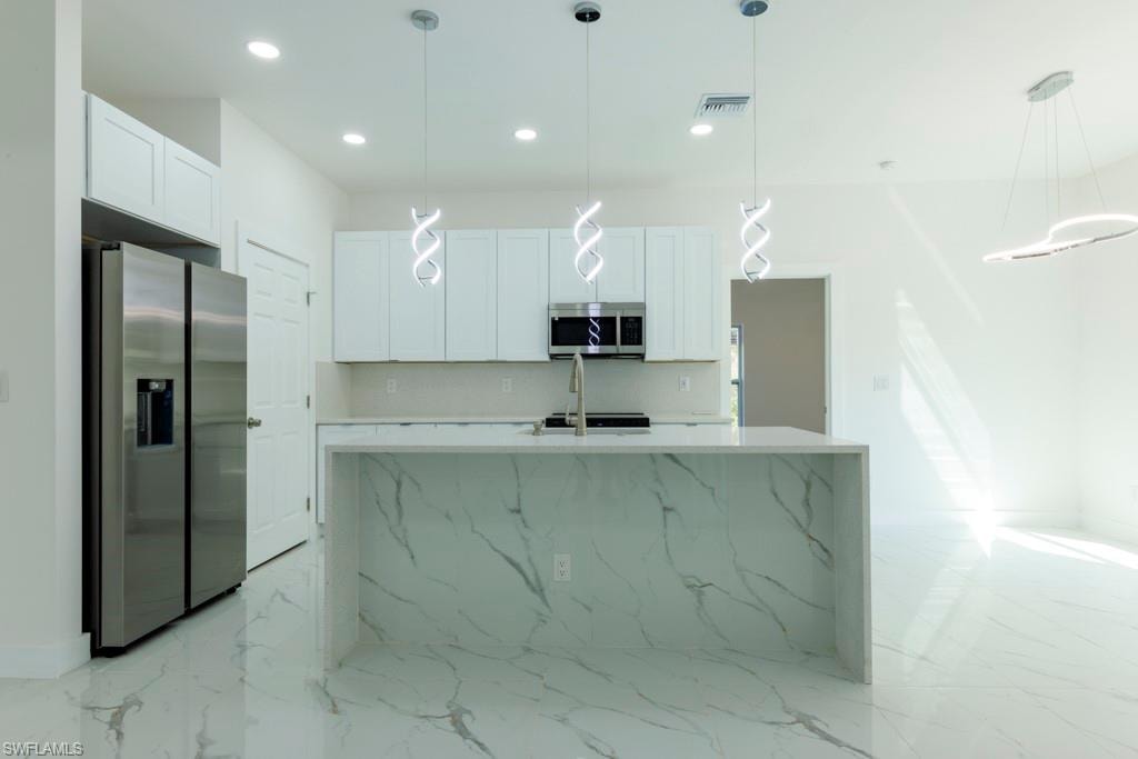 Modern kitchen featuring a waterfall island with a marbled finish, white cabinetry, stainless steel appliances, and sleek pendant lighting