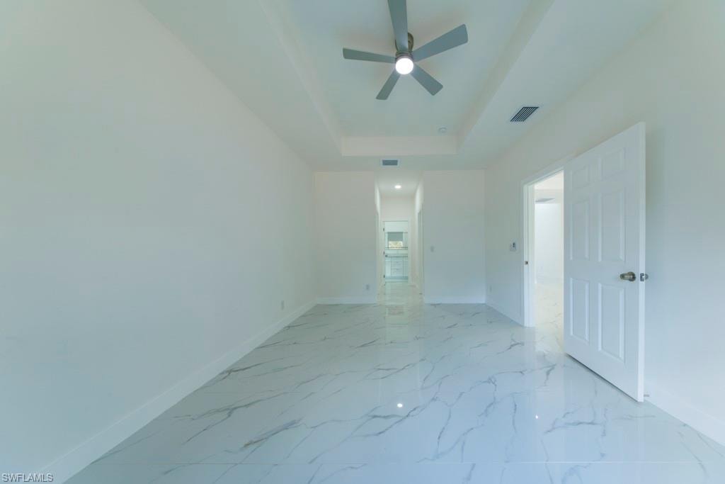 Spacious room featuring large format tile flooring, a tray ceiling, and a modern ceiling fan