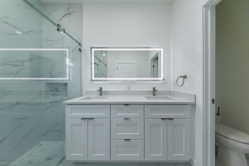 Dual vanity with white cabinetry and integrated sinks, illuminated mirror, and a spacious glass-enclosed shower featuring large format tile