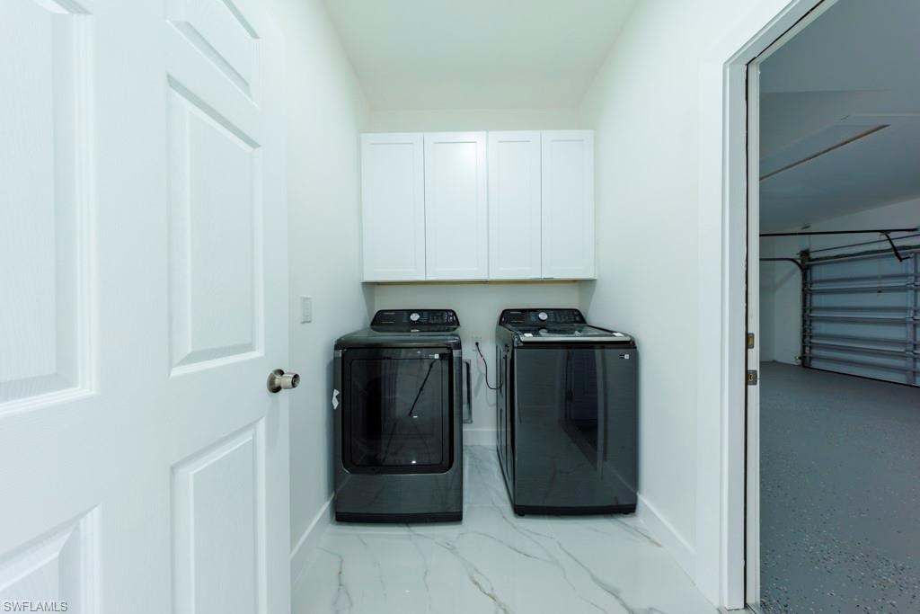 Laundry area featuring white cabinetry with brushed chrome pulls, a white door with paneling, and white marble-look flooring