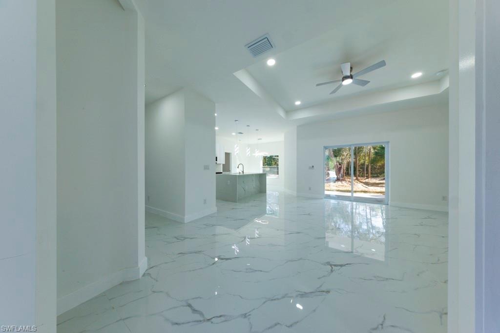 Spacious interior featuring large format marble-look tile flooring, a tray ceiling with recessed lighting and a ceiling fan, and sliding glass doors