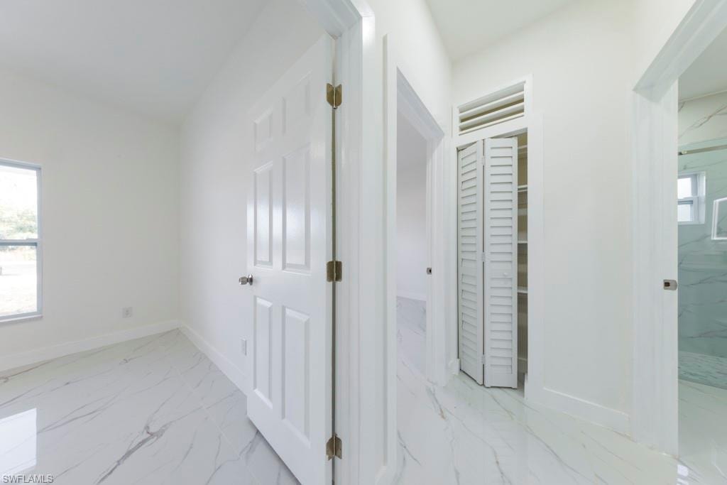 Interior hallway featuring white panel doors, white walls, and marble-finish tile flooring