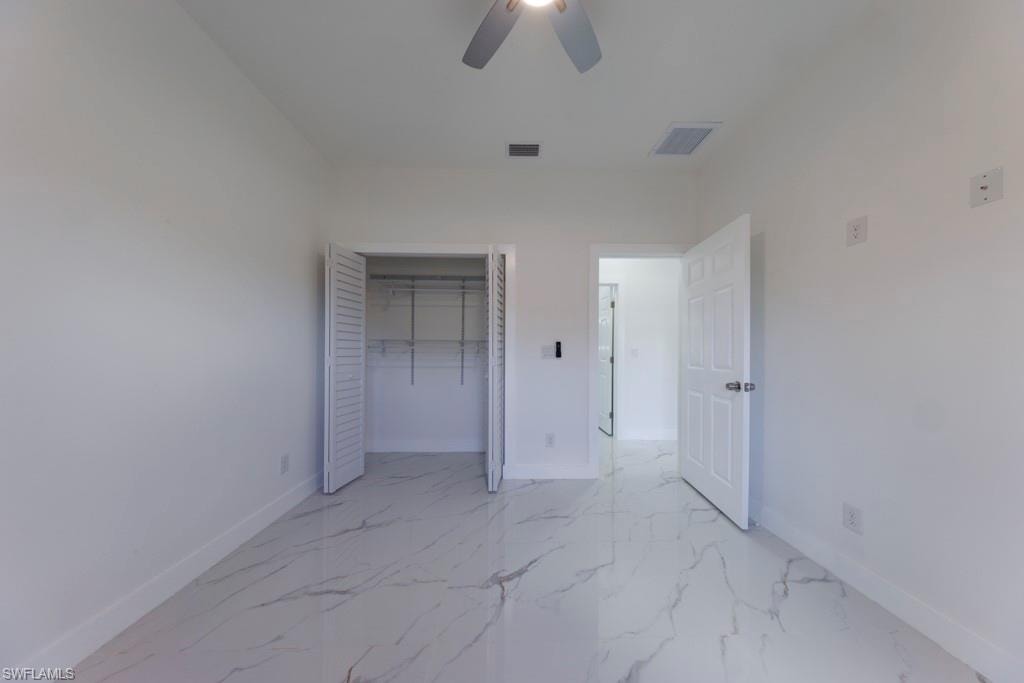 Bright room featuring large format tile flooring, a louvered bifold closet, white walls, a ceiling fan, and a paneled door