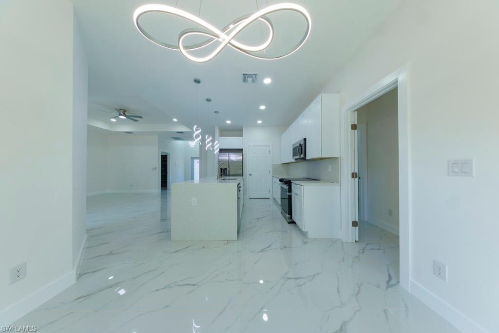 Open-concept kitchen and living area featuring a large center island with pendant lighting, white cabinetry, integrated appliances, and polished tile flooring