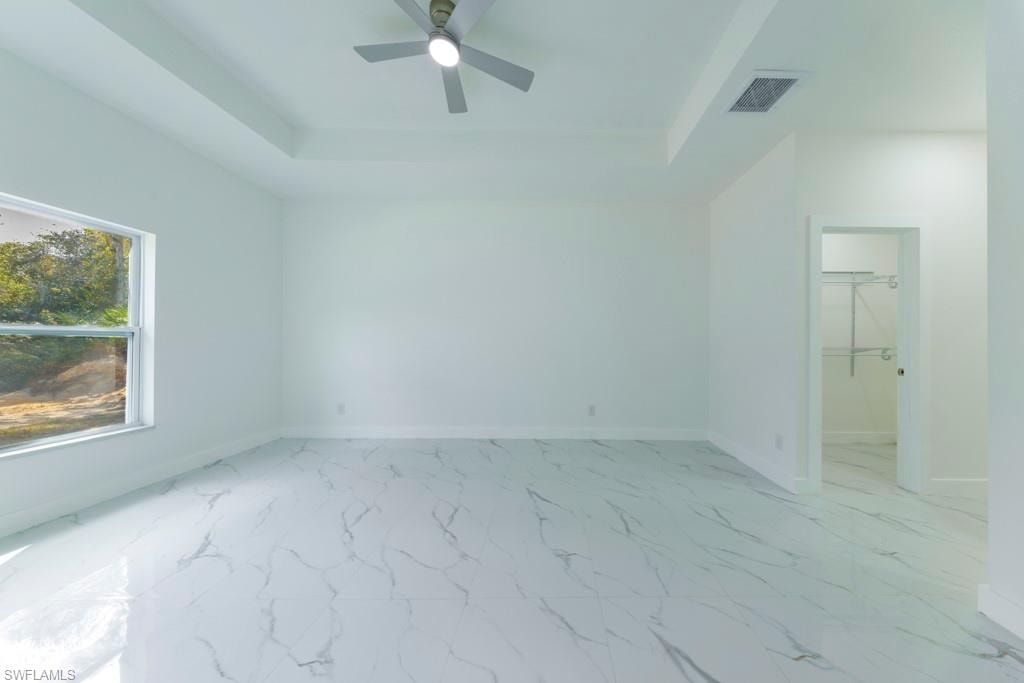 Spacious room featuring white tile flooring with a marble-effect pattern, tray ceiling with a modern ceiling fan, and a large window