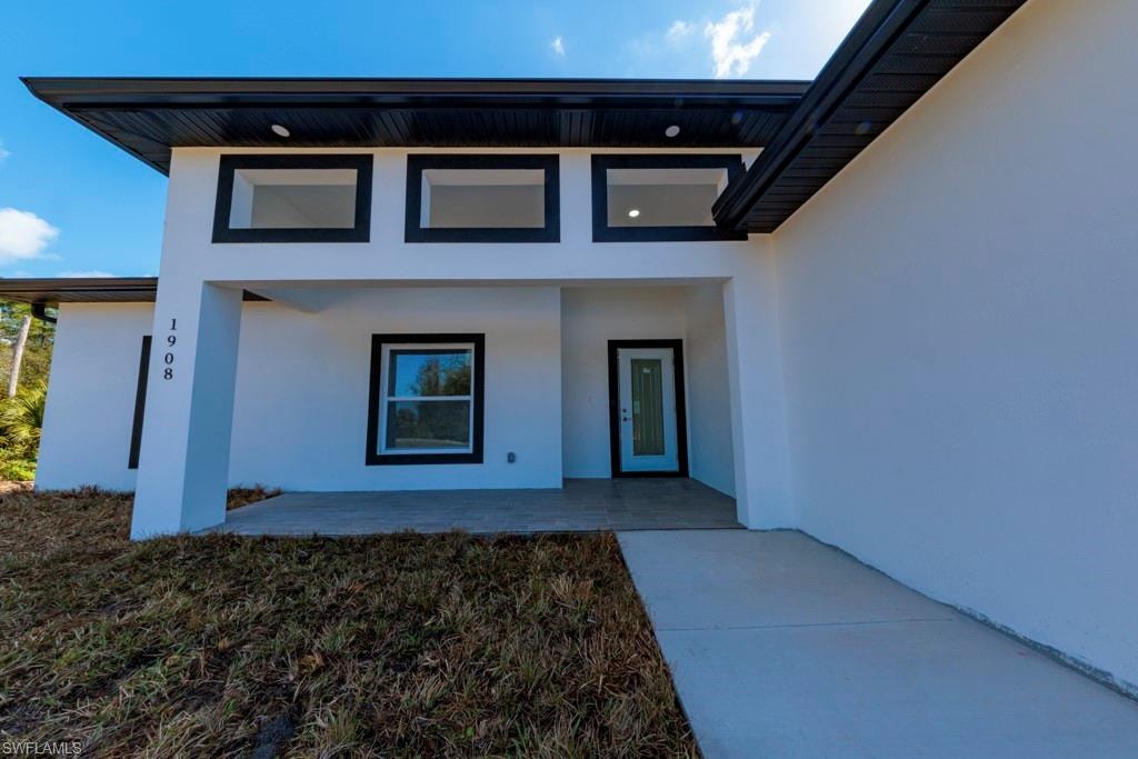 Modern exterior featuring a white stucco facade with black trim accents, a flat roofline, a covered entryway, and a prominent front door with a frosted glass insert