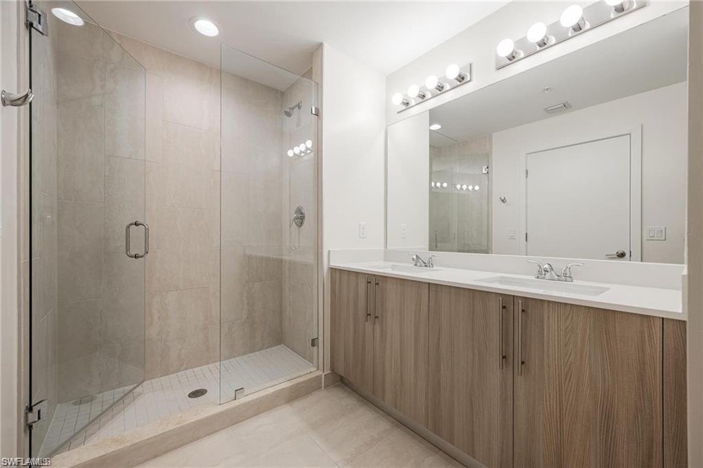 Bathroom with tile patterned floors, a sink, double vanity, and a stall shower
