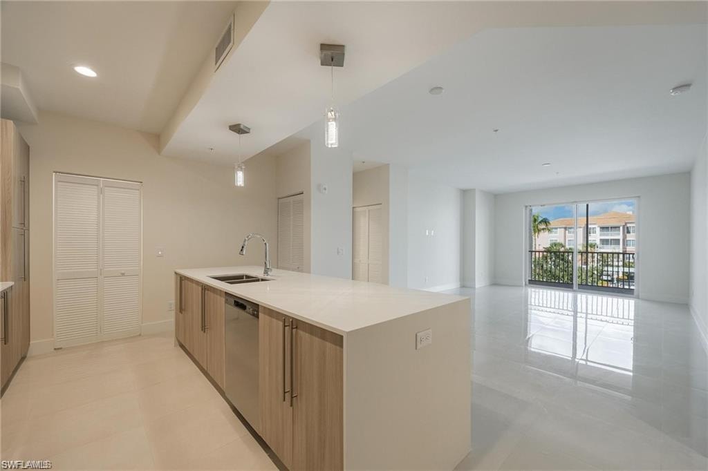 Kitchen featuring light countertops, a sink, open floor plan, dishwasher, and decorative light fixtures