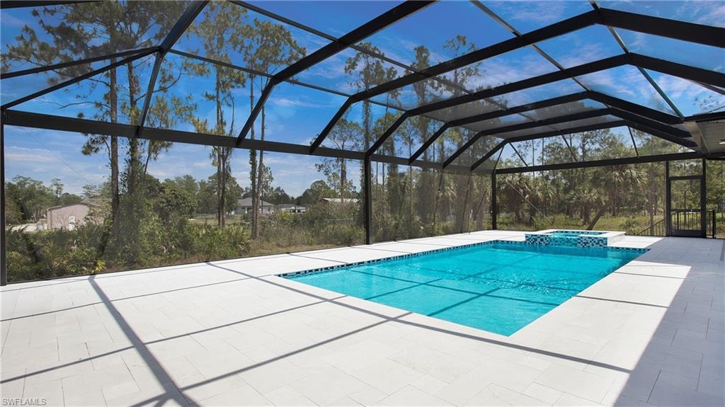 Expansive screened enclosure featuring a rectangular pool with an integrated spa, set against a backdrop of mature trees and open skies