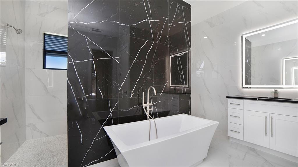 Contemporary bathroom featuring a freestanding soaking tub, a black tiled accent wall, and a custom vanity with an illuminated mirror