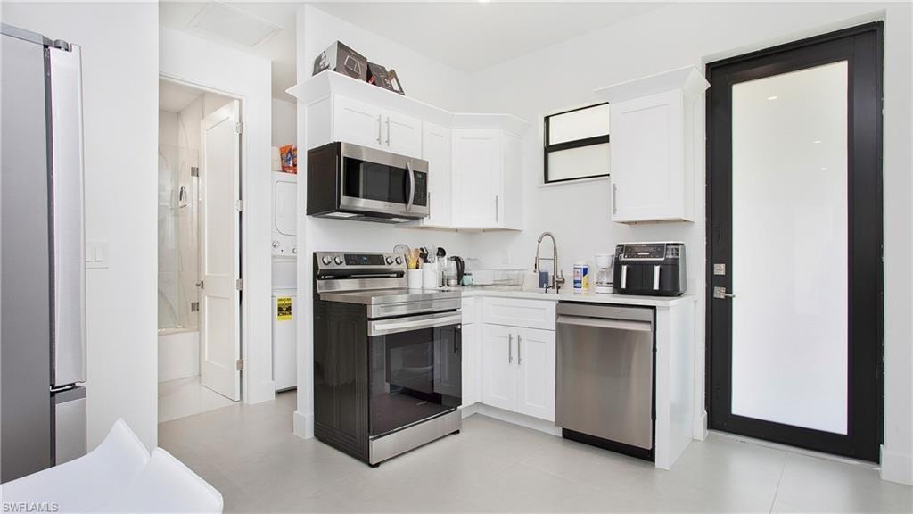 Contemporary kitchen featuring white cabinetry, stainless steel appliances, a white solid surface countertop, and a full-light exterior door with black trim
