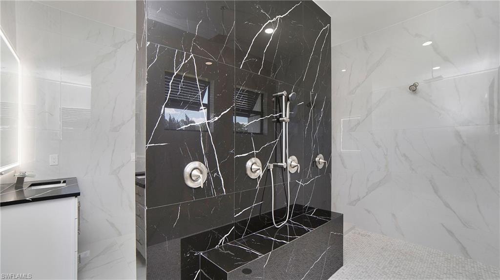 Luxurious shower featuring black marbled wall tiling with white veining, a built-in shower bench, and a brushed nickel shower system