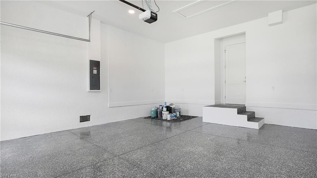 Spacious garage featuring a durable epoxy-coated concrete floor, bright white walls, a built-in step entry, and overhead garage door opener