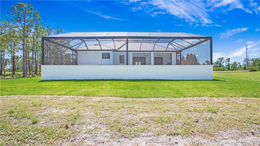 Rear exterior featuring a large screened lanai, a white concrete privacy wall, and a metal roof