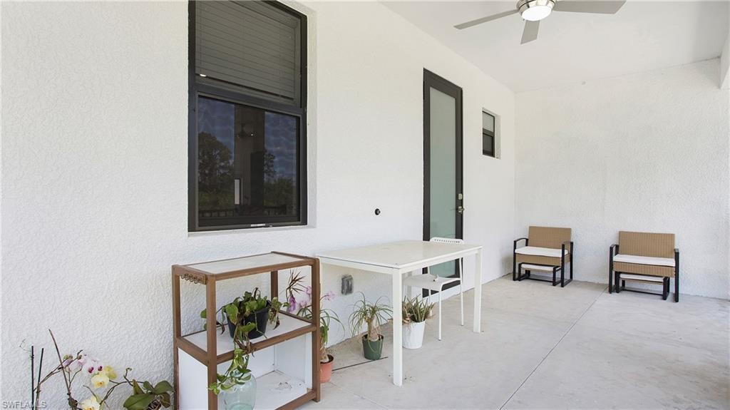 Outdoor patio space featuring a contemporary ceiling fan with integrated lighting, durable concrete flooring, and a dark-framed glass door
