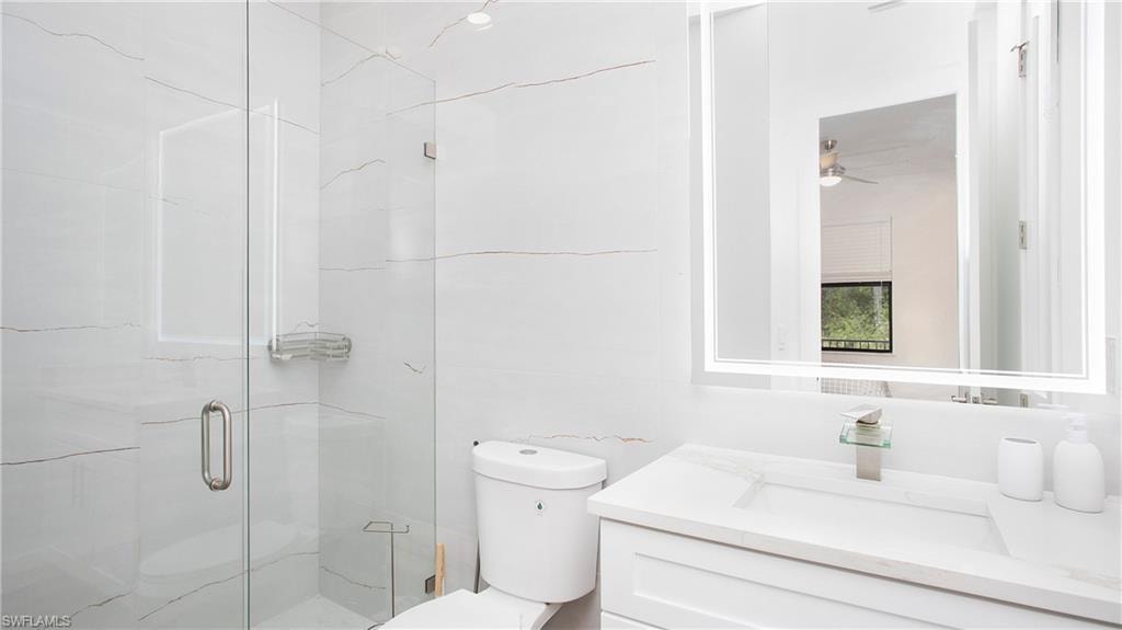 Bathroom featuring a glass-enclosed shower, white marble-look wall tiling, a modern vanity with integrated sink, a rectangular illuminated mirror, and a contemporary toilet