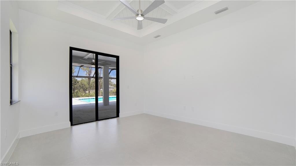Spacious room featuring white walls, a coffered ceiling with a ceiling fan, and light-toned flooring