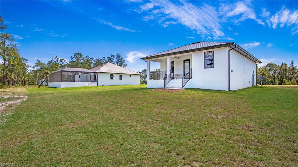 Expansive property featuring two structures, a screened enclosure, a covered porch with railings, and a large grassy area