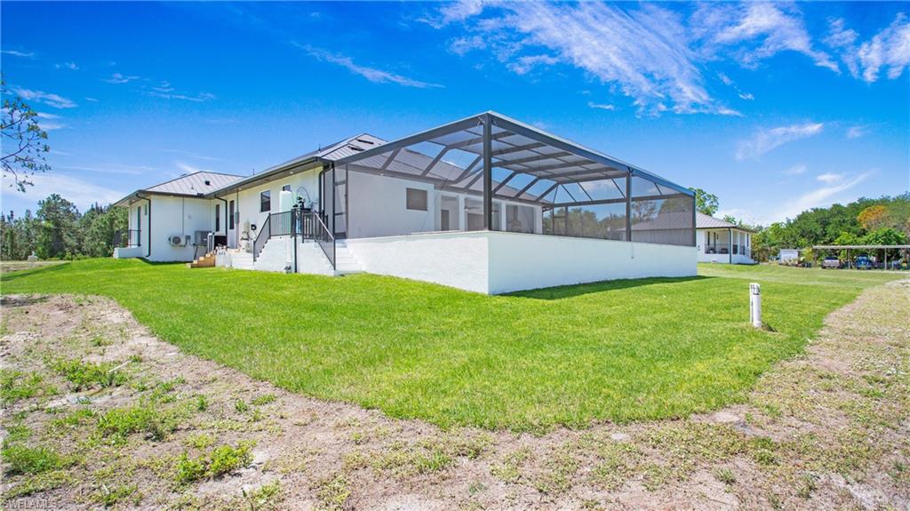 Expansive green lawn surrounds a white-stucco exterior home featuring a screened-in enclosure, a metal roof, and a raised patio with stairs