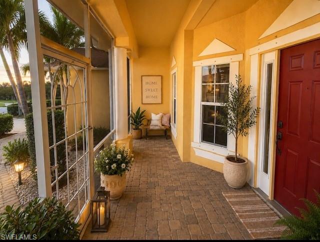 Screened entryway featuring a red front door with sidelight, yellow stucco exterior, brick paver flooring, and decorative windows