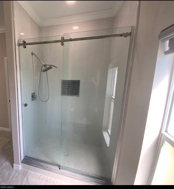 Glass-enclosed shower featuring a sliding door, rain showerhead, handheld shower, and an integrated tiled niche