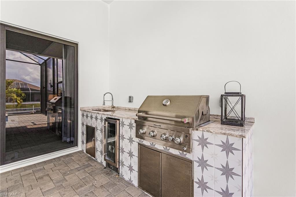 Outdoor kitchen featuring an integrated stainless steel grill, beverage refrigerator, and sink