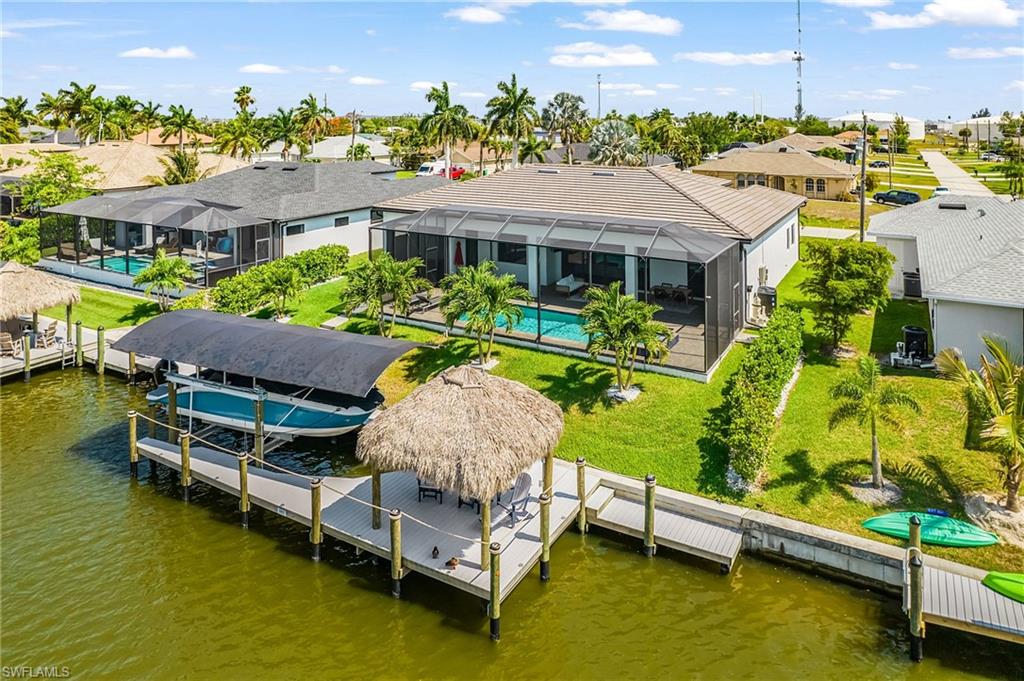 Waterfront property featuring a private dock with a covered boat lift, an additional dock with a tiki hut, a screened-in lanai, and an in-ground swimming pool
